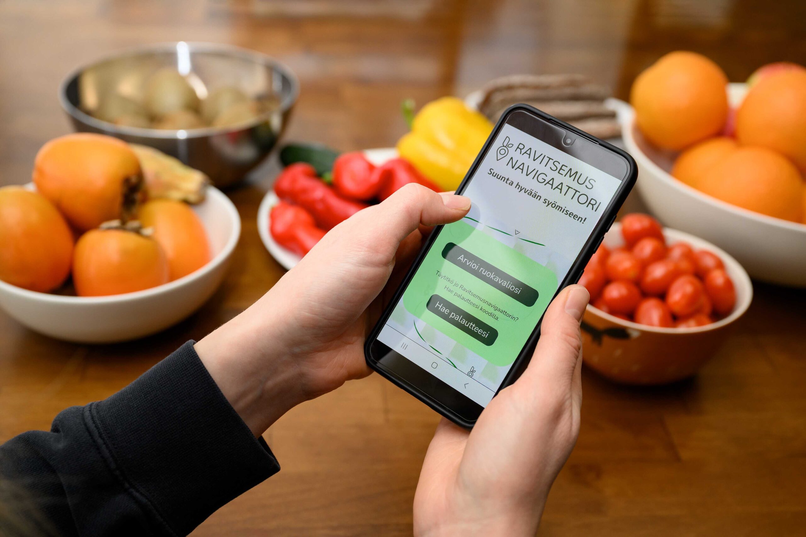 A phone being hand held and showing the ravitsemusnavigaattori website. In the background there are some vegetables held in plates.